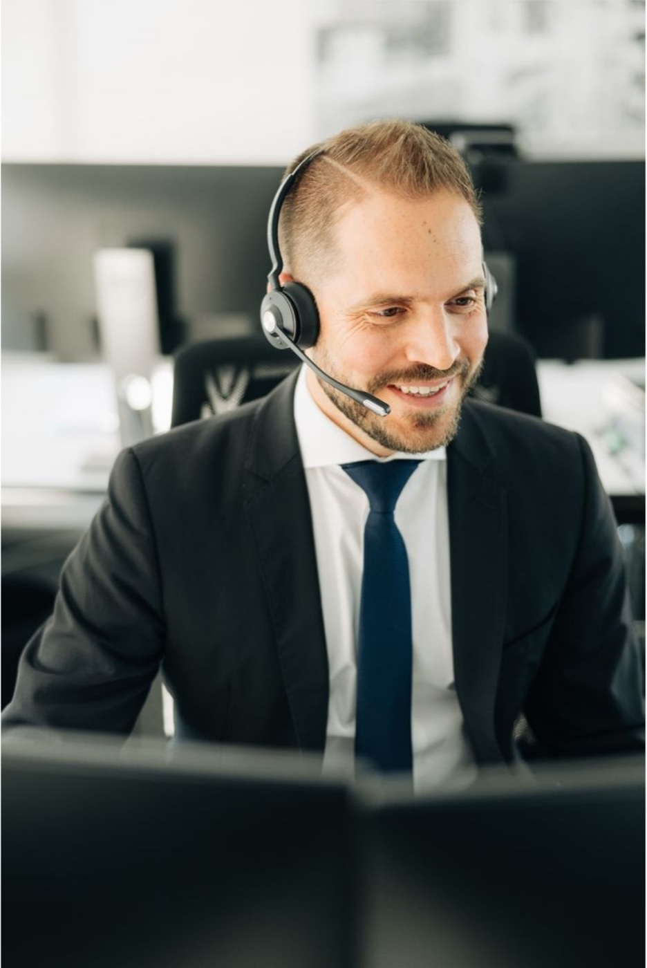 Un agente con auriculares en su escritorio, sonriendo frente a la pantalla.