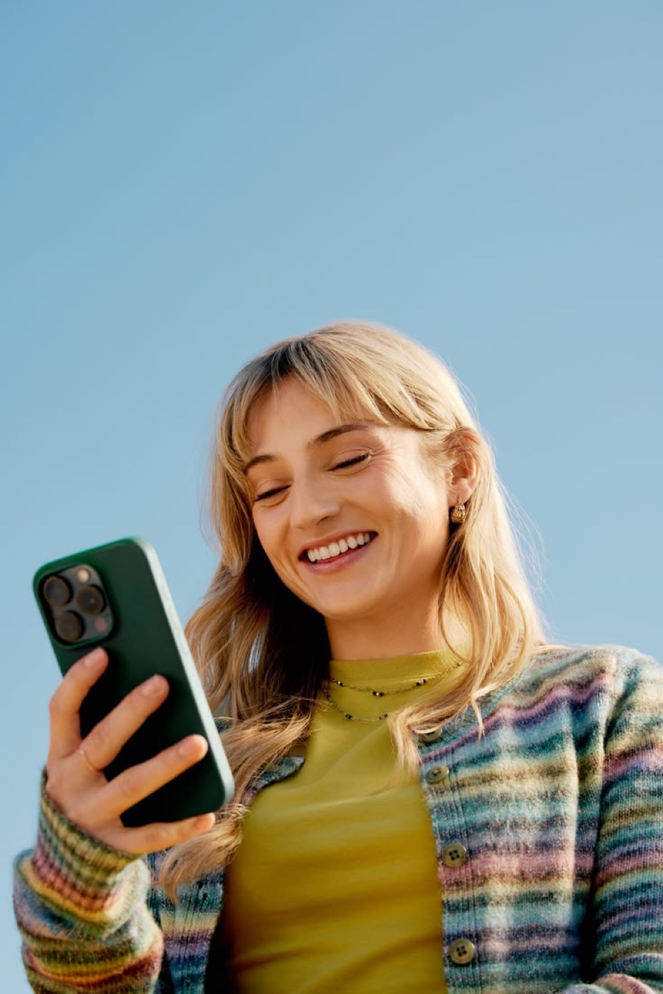 Una clienta al aire libre, sonriendo mientras mira su teléfono.